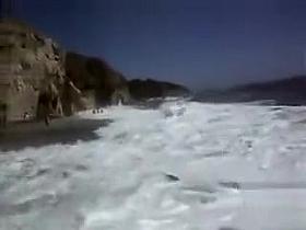 Busty brunette's lower part of a bikini drops as huge waves hit her