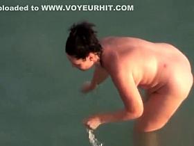 Nude couple in rocky beach taking pictures