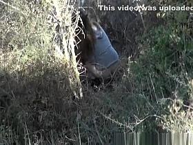 Woman peeing beyond some bushes