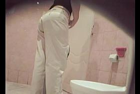 A woman wearing white jeans is pissing in the public toilet